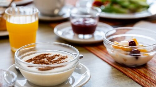 Fahéjjal megszórt tejberizs és gyümölcsös joghurt a reggelizőasztalon.
