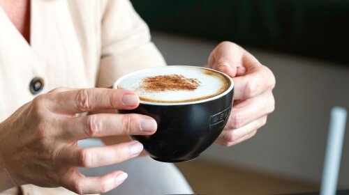 Kezekben tartott cappuccino csésze fahéjjal megszórva.