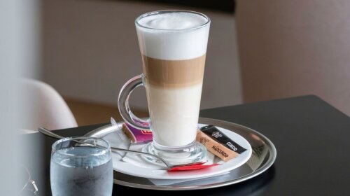 Latte macchiato magas pohárban, tálcán tálalva az asztalnál.