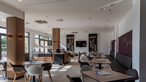 Tágas étterem tér faburkolatú oszlopokkal, Food Garden és italos táblákkal a falon.
